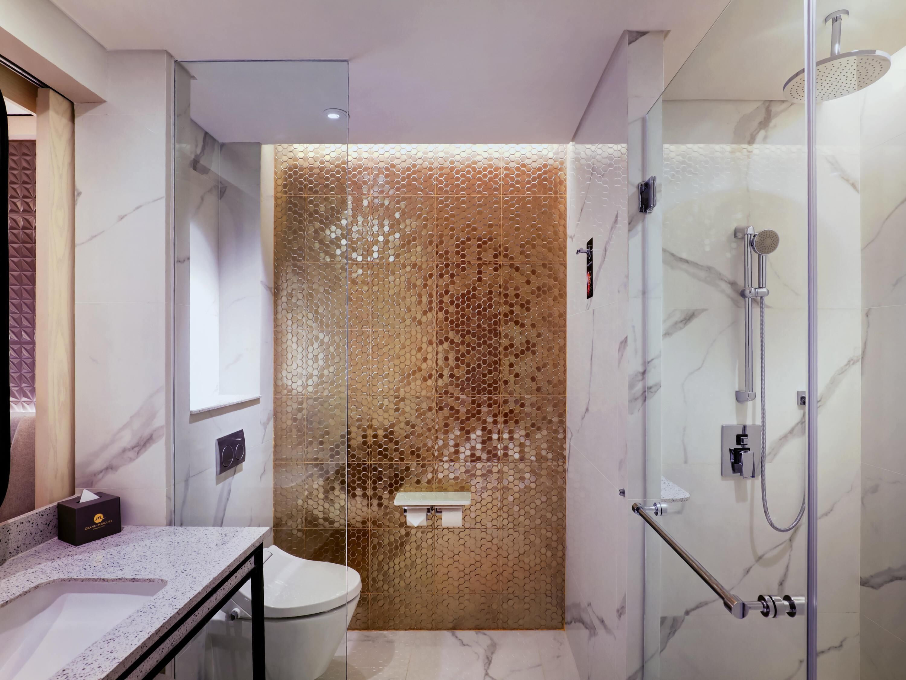A modern bathroom with a glass shower enclosure, a marble-tiled wall, and a toilet with a towel dispenser.