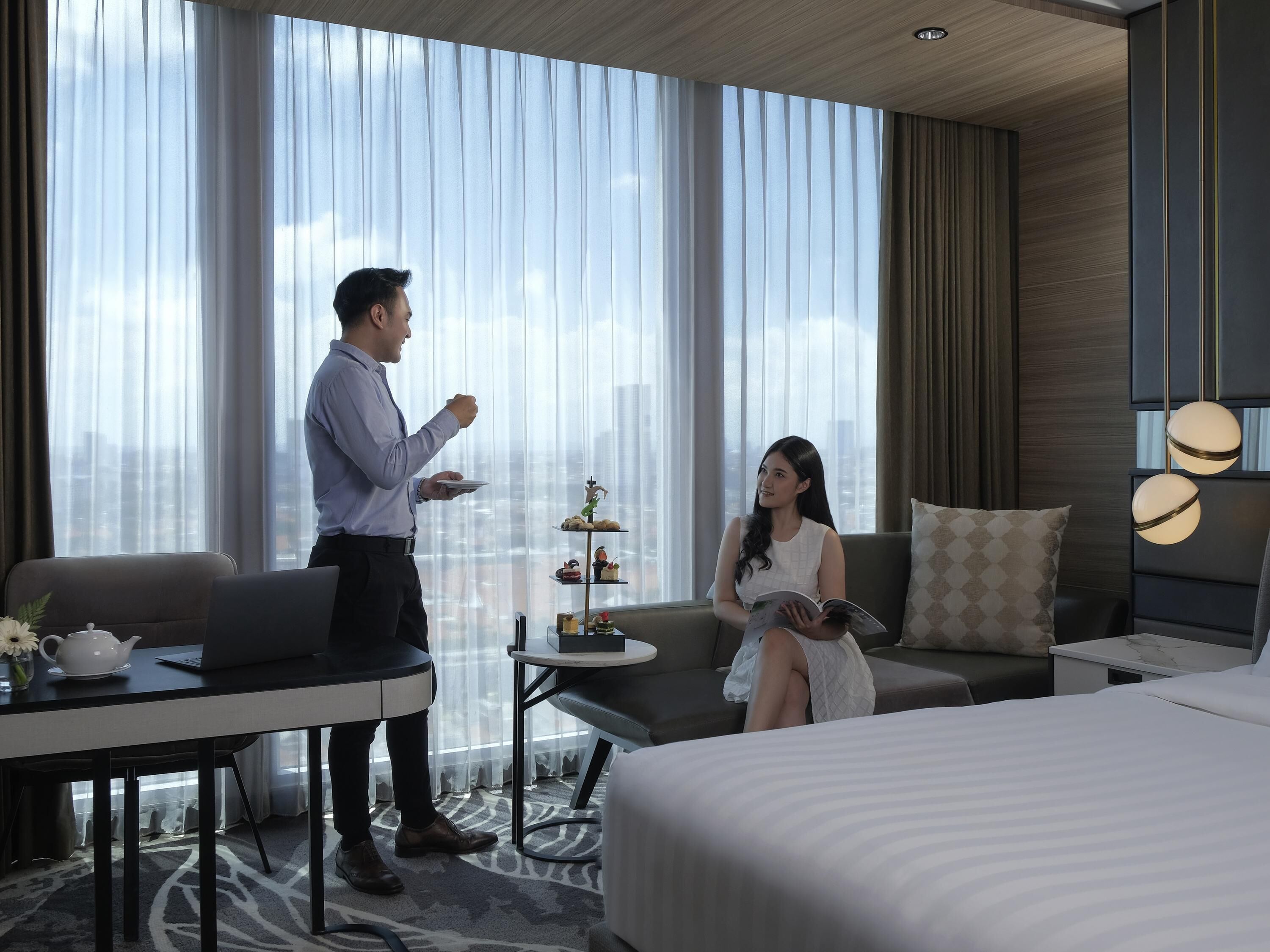 A modern hotel room with a large window, a dining table, a sofa, and a bed.