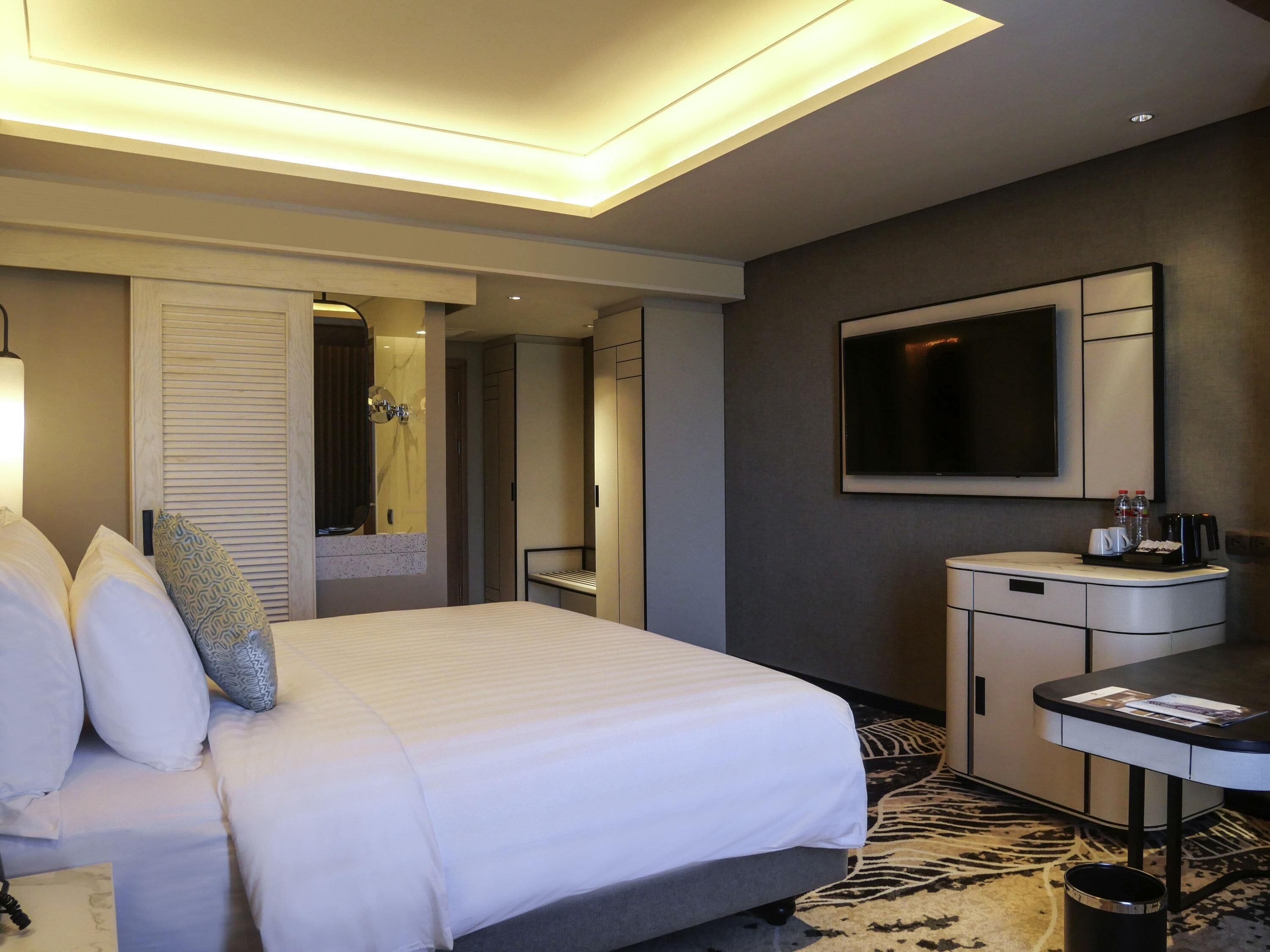 Una habitación de hotel con cama, escritorio, espejo, televisión y alfombra estampada.