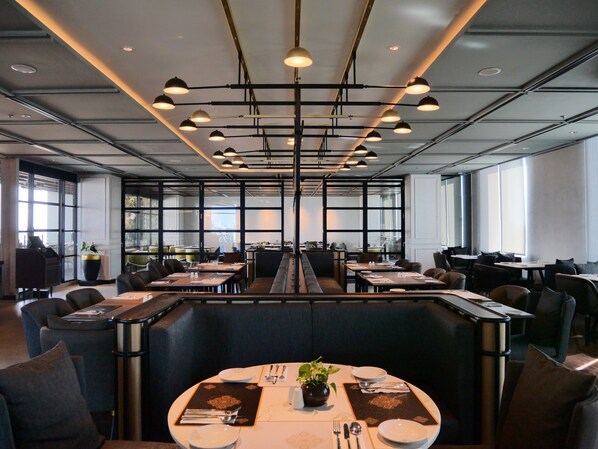 Een modern restaurant met hoge plafonds, hanglampen en een centraal zitgedeelte met een lange tafel.