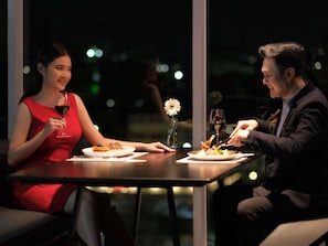 Two people dining at a table with a view of the night sky. - Movenpick Surabaya City (Surabaya)