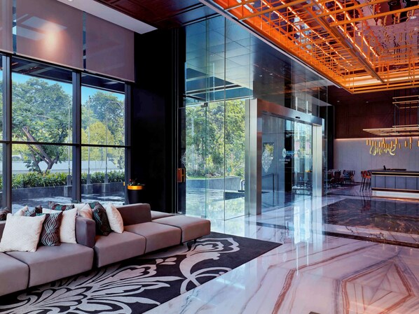 A modern lobby with a sofa, a patterned rug, and a reception desk. - Movenpick Surabaya City (Surabaya)