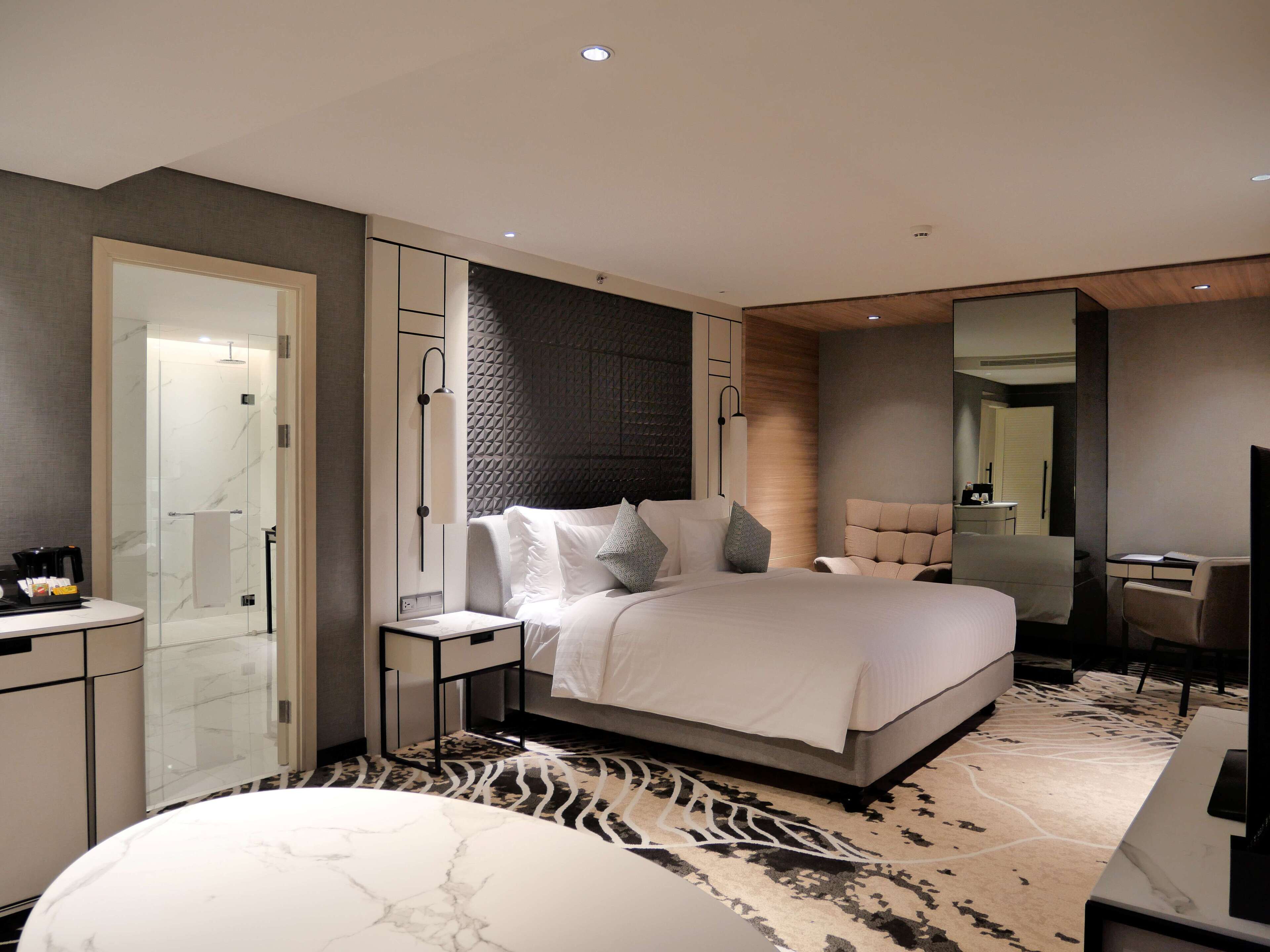 Una habitación de hotel moderna con una cama grande, una zona de estar, un escritorio y un baño.