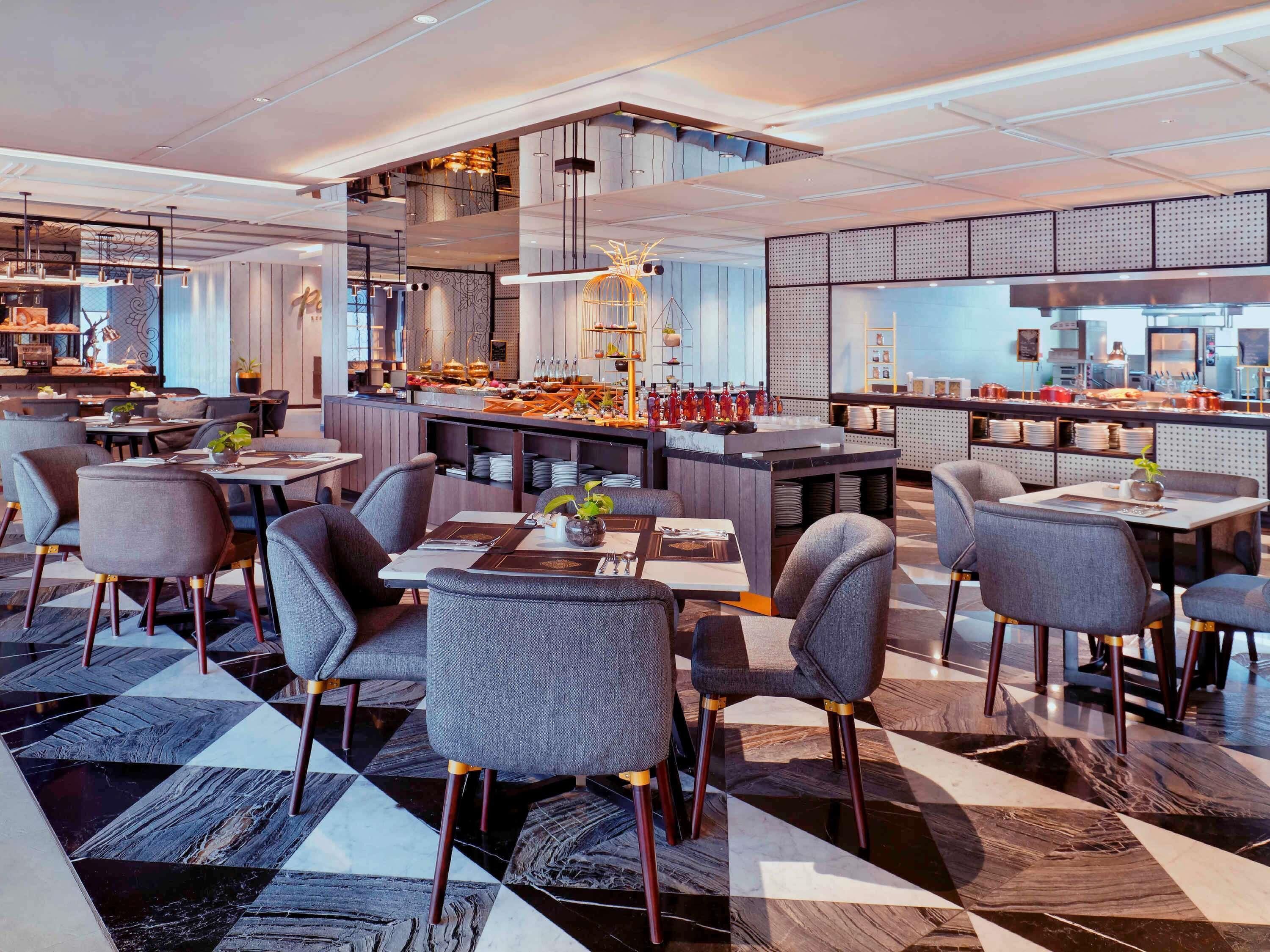 A modern restaurant with a checkered floor, grey upholstered chairs, and a central bar area.