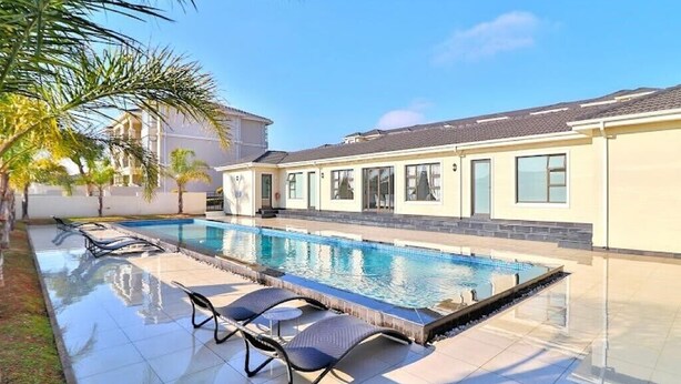 A swimming pool with lounge chairs, a tiled deck, and a building with large windows.