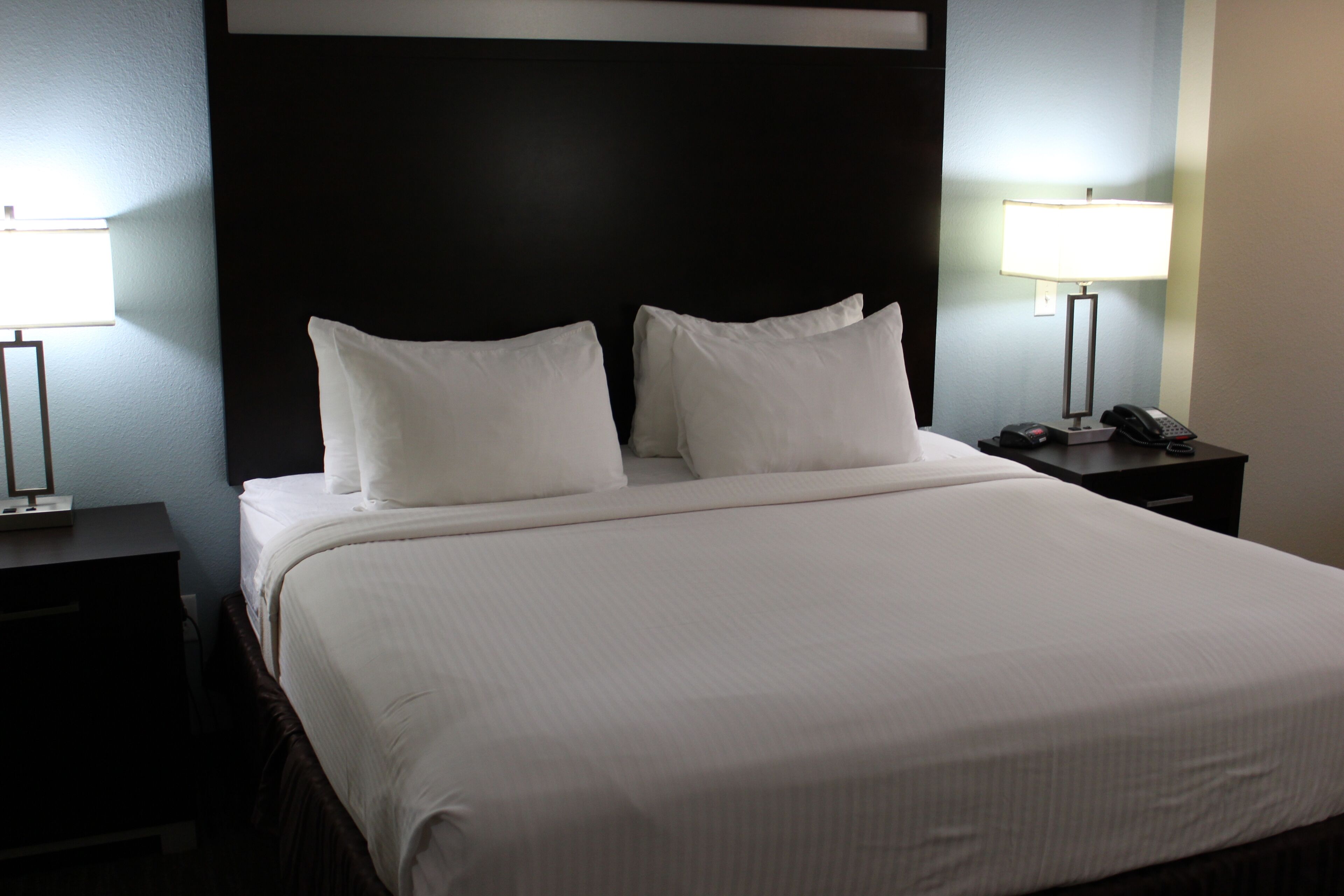 A neatly made bed with white linens, two bedside tables with lamps, and a dark headboard.