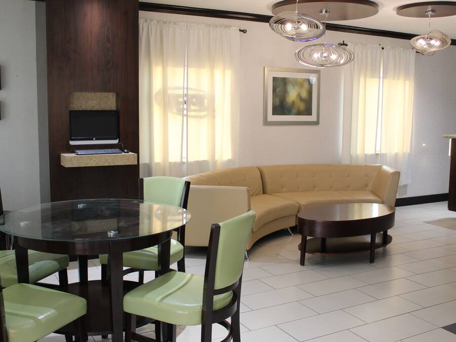 A modern living room with a round glass table, green chairs, a beige sofa, and a flat-screen TV mounted on a wooden panel.