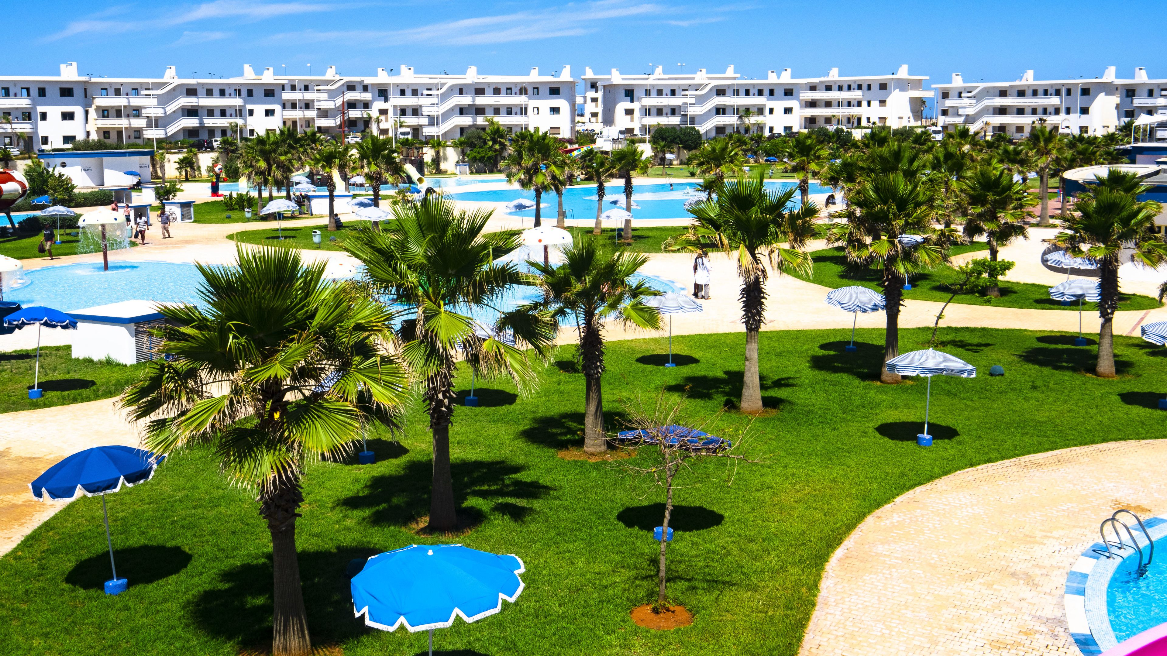 Um resort com várias piscinas, palmeiras e um prédio grande ao fundo.