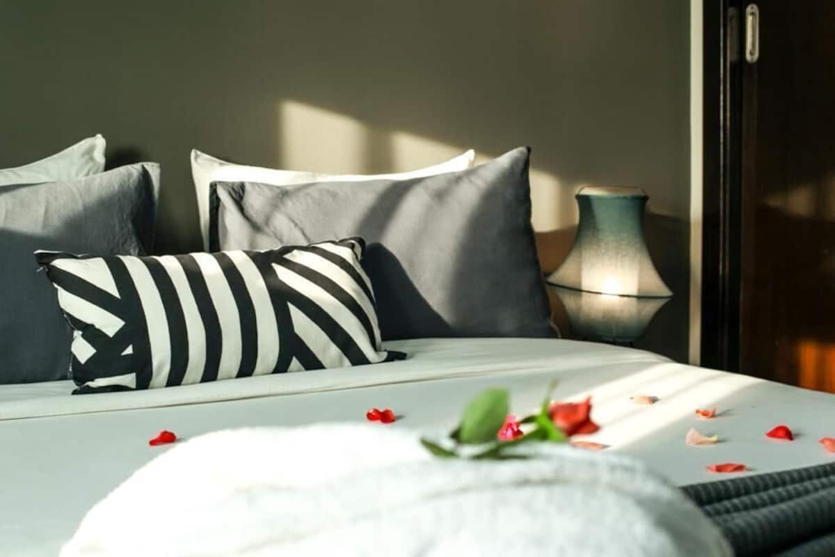 A bed with striped pillows, a vase, and scattered rose petals.