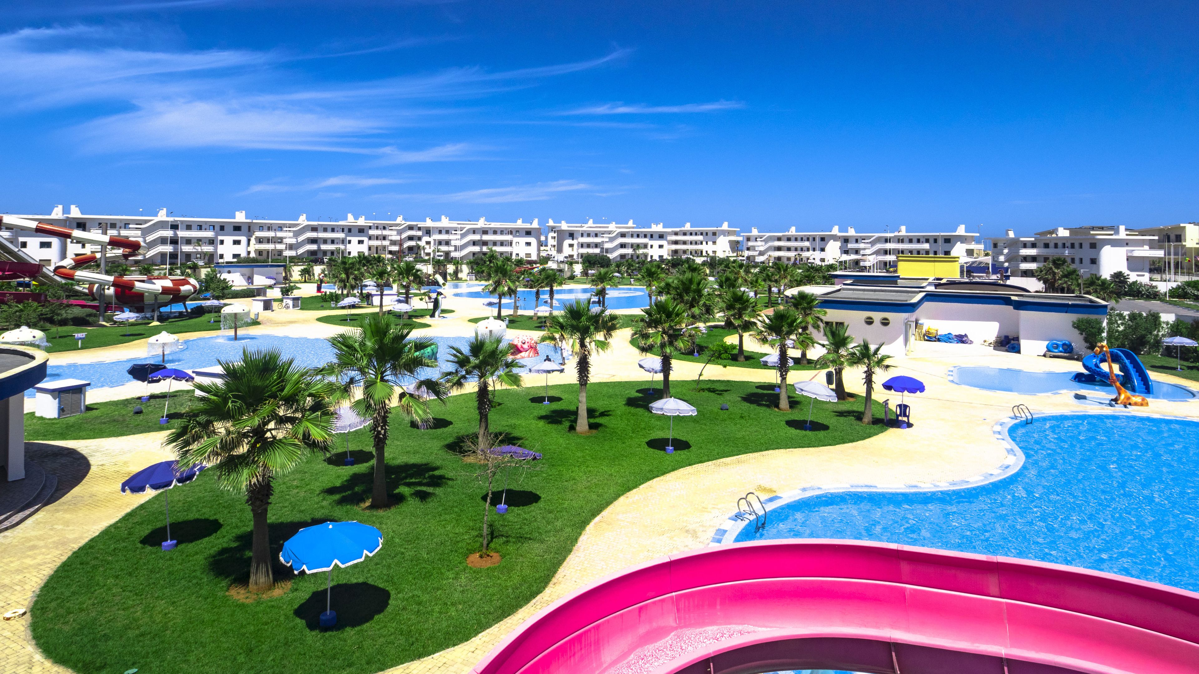 Un complexe hôtelier doté d’une grande piscine, de palmiers et d’un toboggan aquatique.