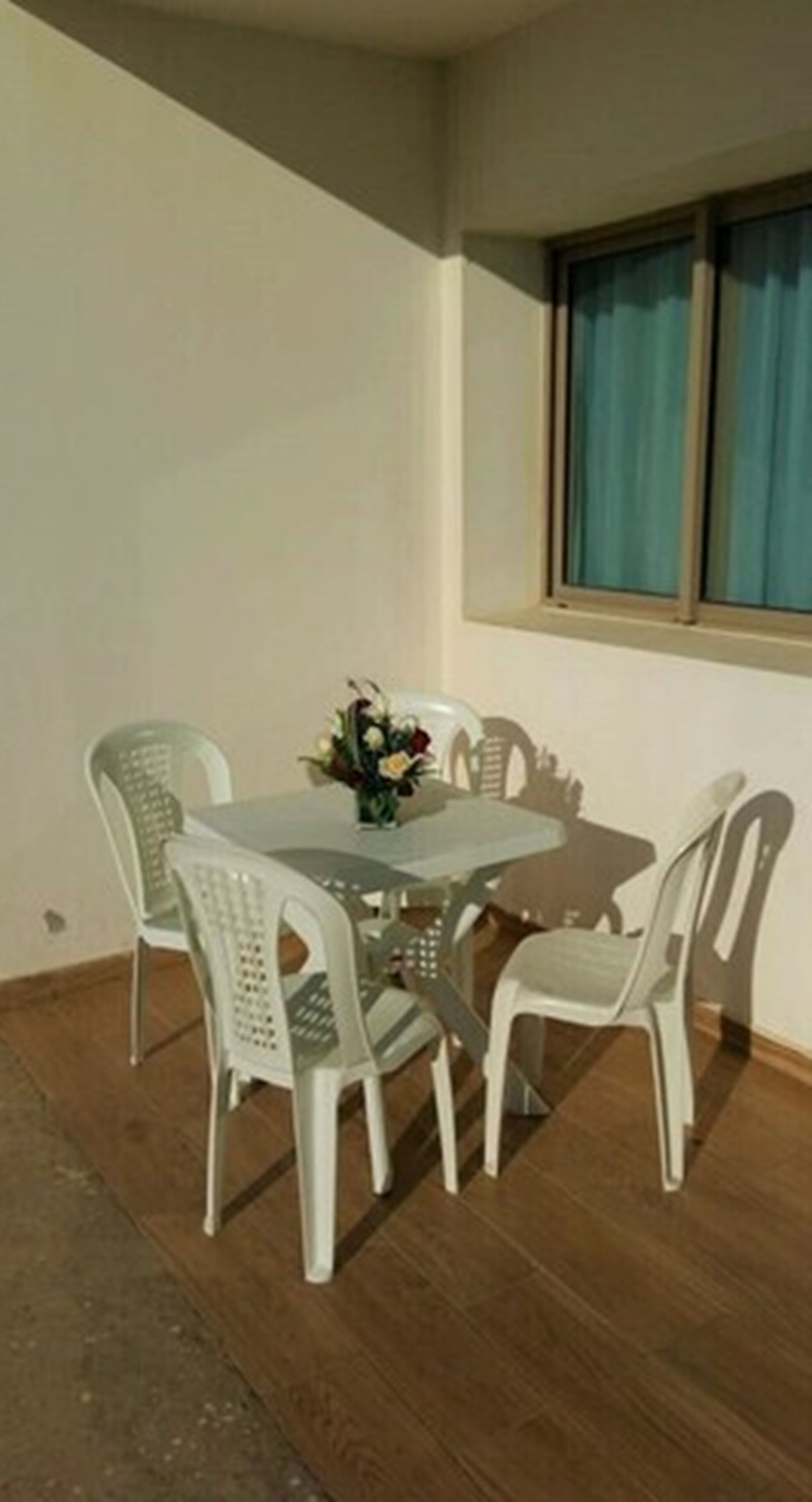 Een eethoek met een tafel en vier stoelen, een vaas met bloemen en een raam met gordijnen.