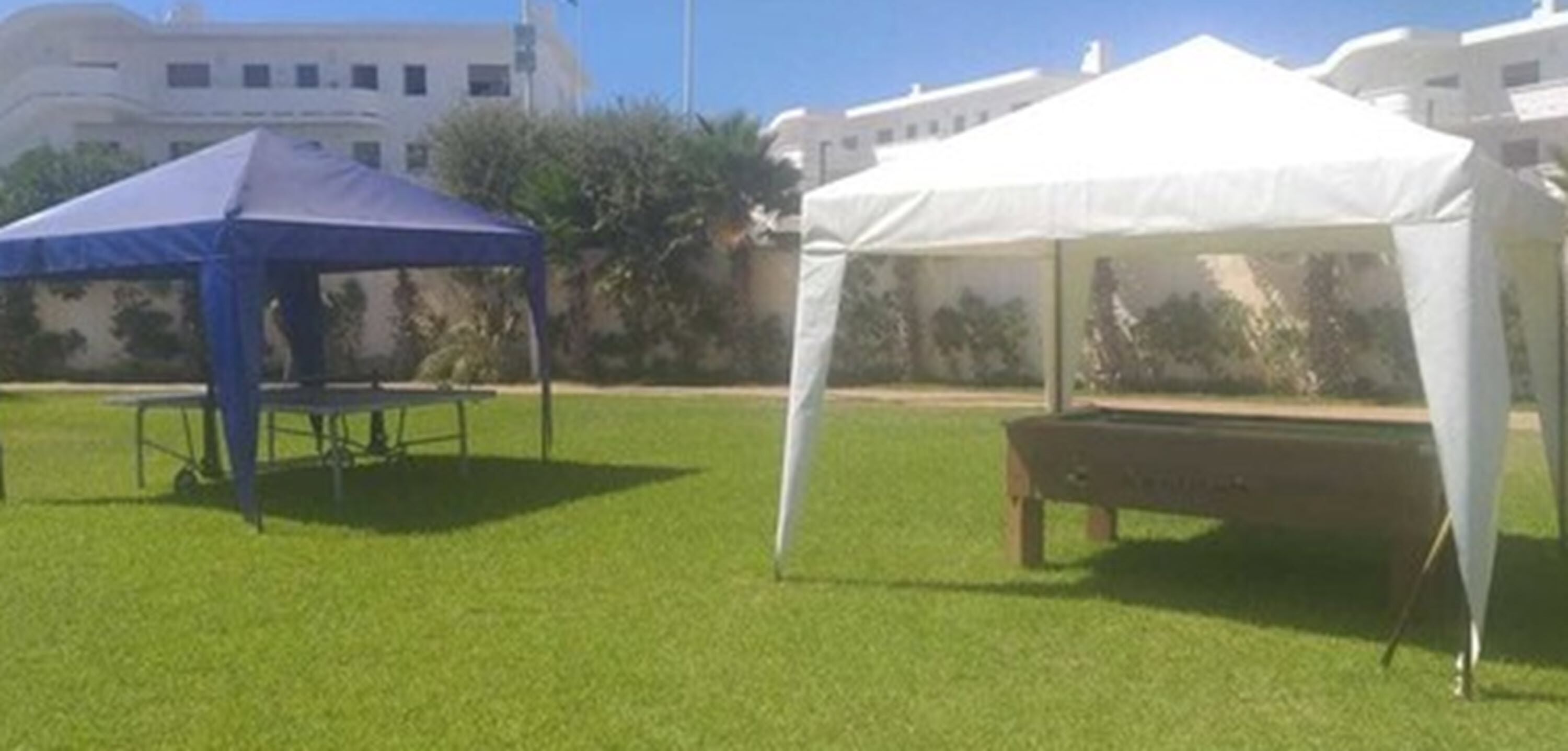 Uma área gramada com uma tenda azul e uma tenda branca.