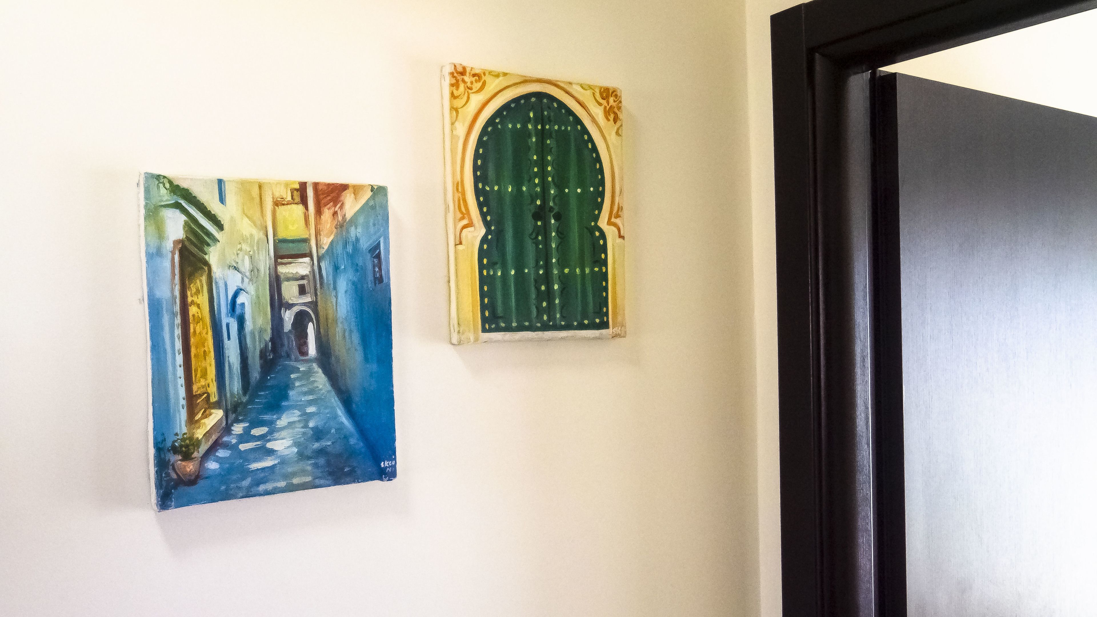 A hallway with a painting of a blue street and a green door.