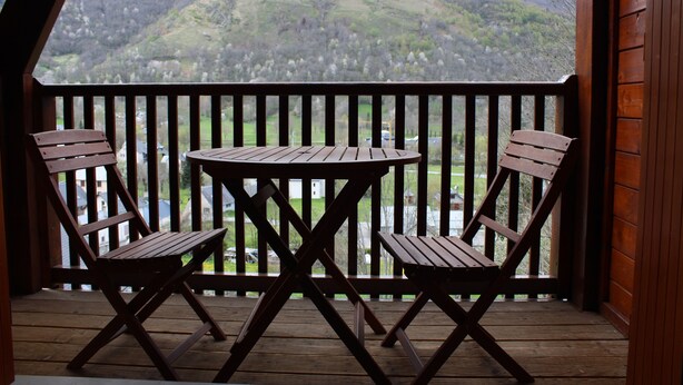 Een houten terras met twee houten stoelen en een tafel, met uitzicht op een glooiend landschap.