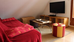 Een gezellige kamer met een bed, een rode plaid, een klein voetenbankje, een televisie en een houten kast.