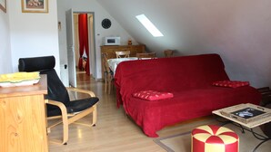 Een gezellige woonkamer met een rode bank, houten meubels, een eethoek met een tafel en stoelen, en een keuken met een magnetron.