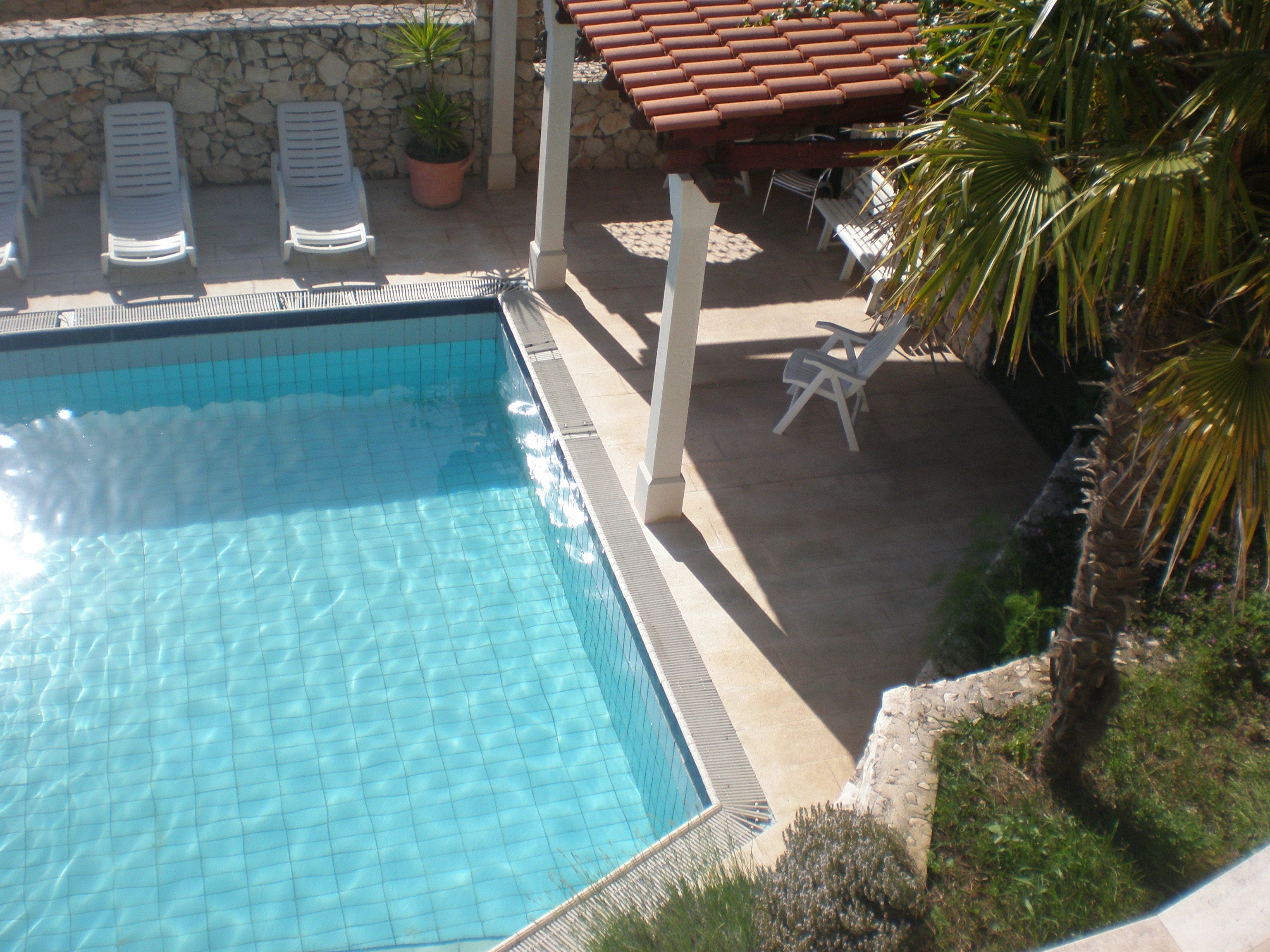 Una piscina con bordes de azulejos, sillas de descanso y una pared de piedra con una planta en maceta.