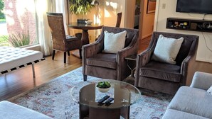 A living room with a large sofa, two armchairs, a glass coffee table, and a TV mounted on the wall.