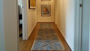 A hallway with wooden flooring, two framed paintings on the walls, and a light fixture on the ceiling.