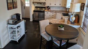 A compact kitchen with white cabinets, a stove, a sink, and a dining area with a round table and chairs.