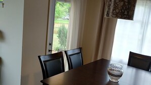 A dining room with a wooden table, four chairs, a glass bowl, and a view of a garden through a door.