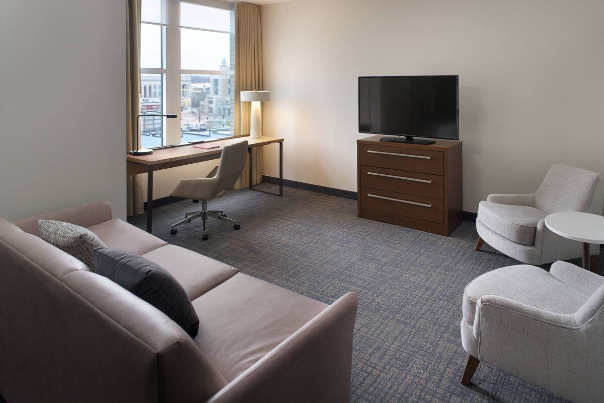 Een hotelkamer met een bank, een bureau met lamp, een televisie en een stoel.