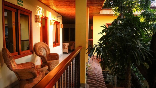 A balcony with wicker chairs, a wooden railing, and a large potted plant. - Hotel Casa Vinculos (Esteli)