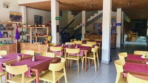 A dining area with wooden tables and yellow chairs, a staircase, and a kitchen area visible in the background. - Hotel Casa Vinculos (Esteli)