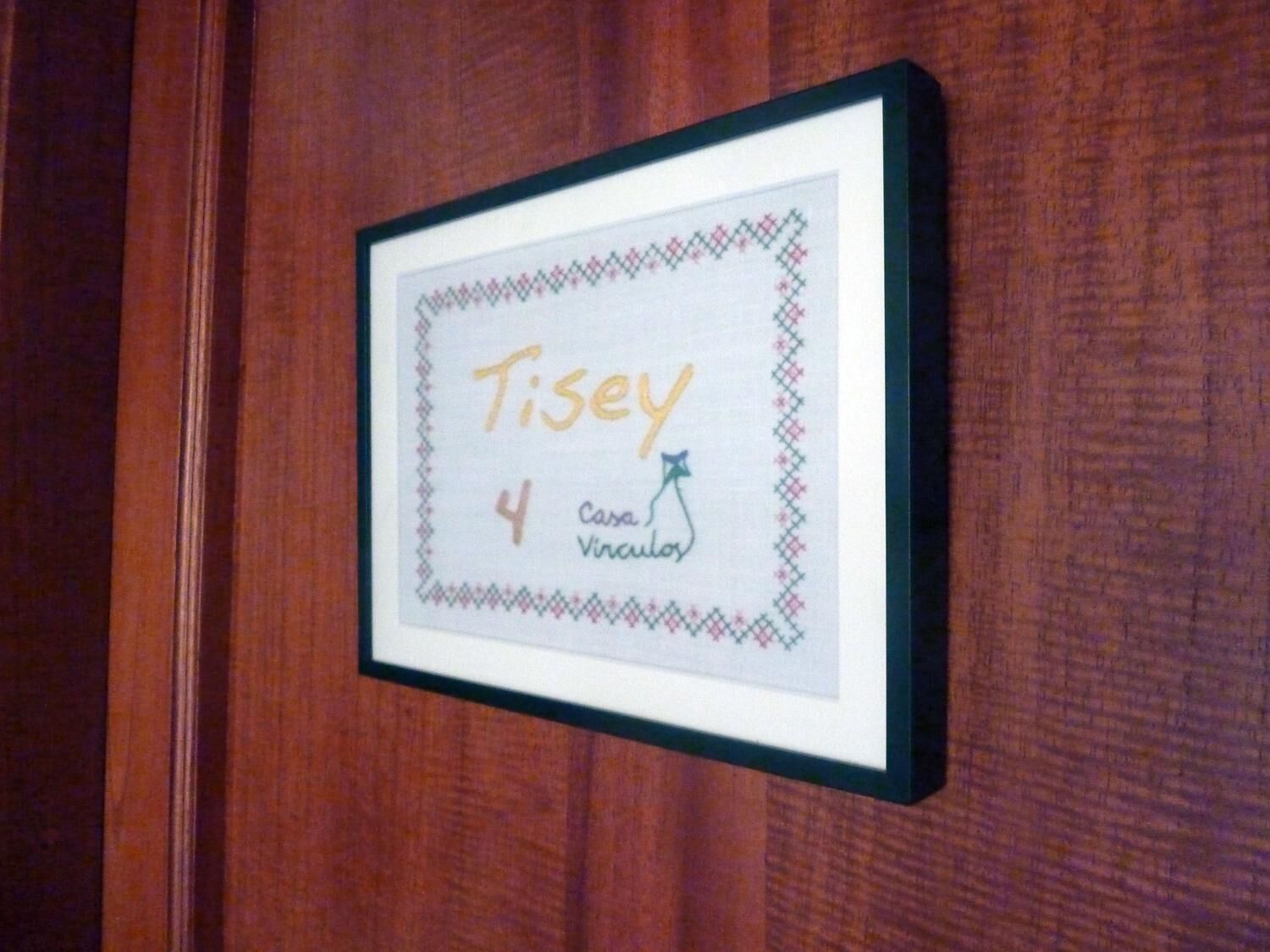 Una obra de arte en marco con el nombre "Tisey" y el número "4", sobre una superficie de madera.