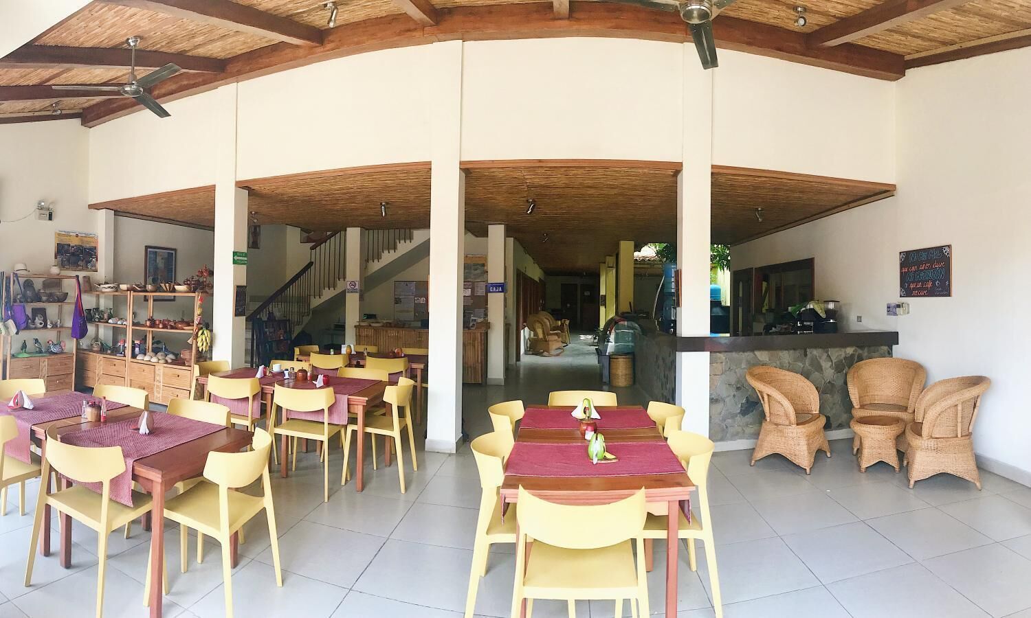 A spacious indoor dining area with multiple tables and chairs, a staircase leading to an upper level, and a bar area with wicker chairs.