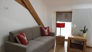 A modern living room with a grey sofa, red and white decorative pillows, a wooden side table with a plant, and a red floor lamp. - Hotel Ristorante-Pizzeria Al Cervo (Magre sulla Strada del Vino)