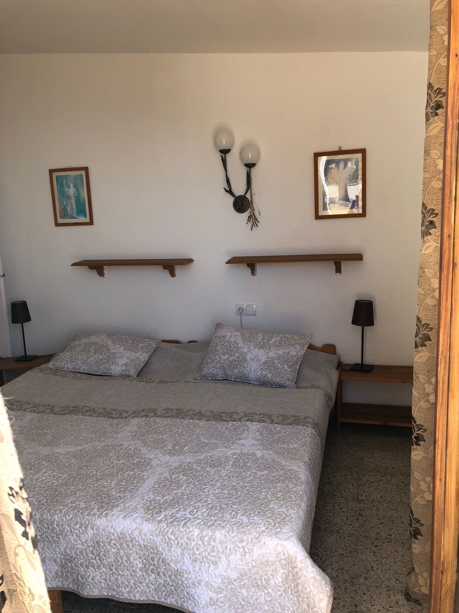 A bedroom with a large bed, two bedside tables, a wall-mounted clock, and two framed pictures.