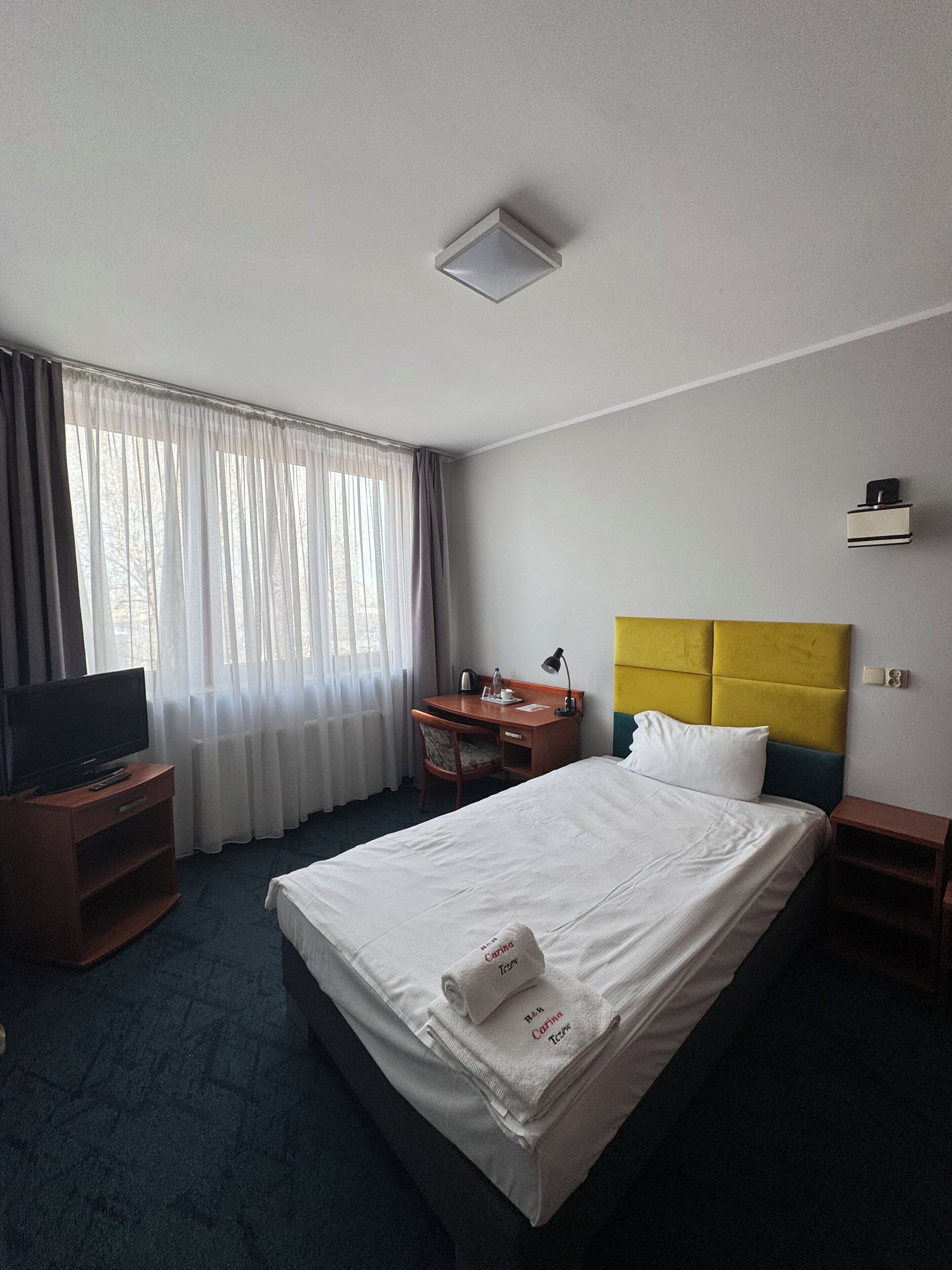 A hotel room with a bed, a desk, a television, and a window with curtains.