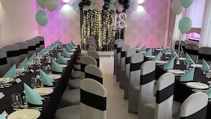 A banquet hall with rows of tables set for a formal event, chairs with black and white sashes, and a decorative backdrop with balloons and lights. - Hotel Carina (Tczew)