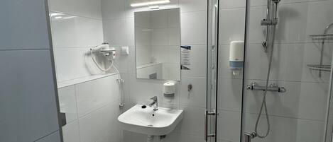 Un baño moderno con cabina de ducha de vidrio, un lavamanos blanco y un inodoro.