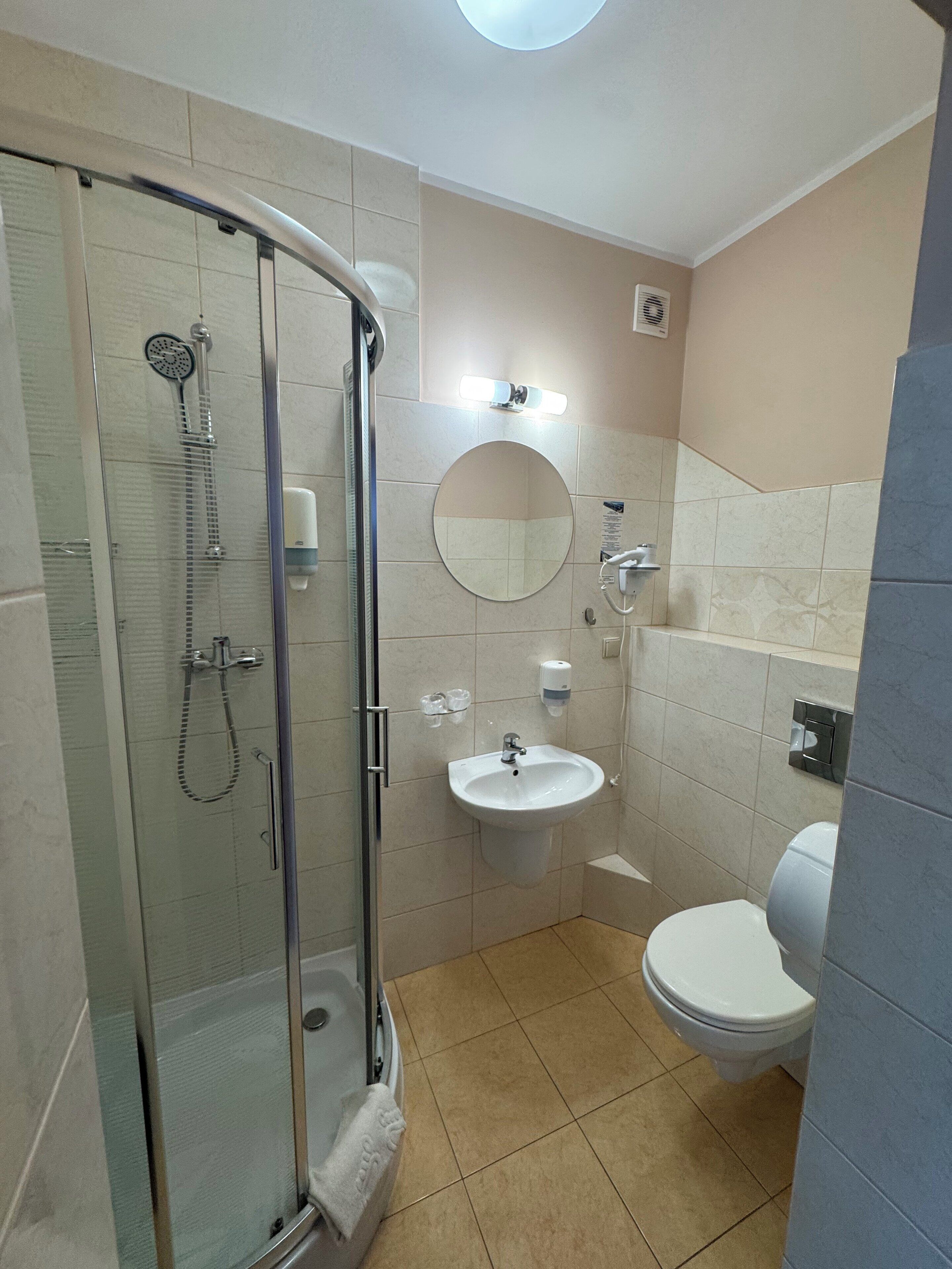 Un baño moderno con ducha envuelta en vidrio, lavamanos, inodoro y espejo.