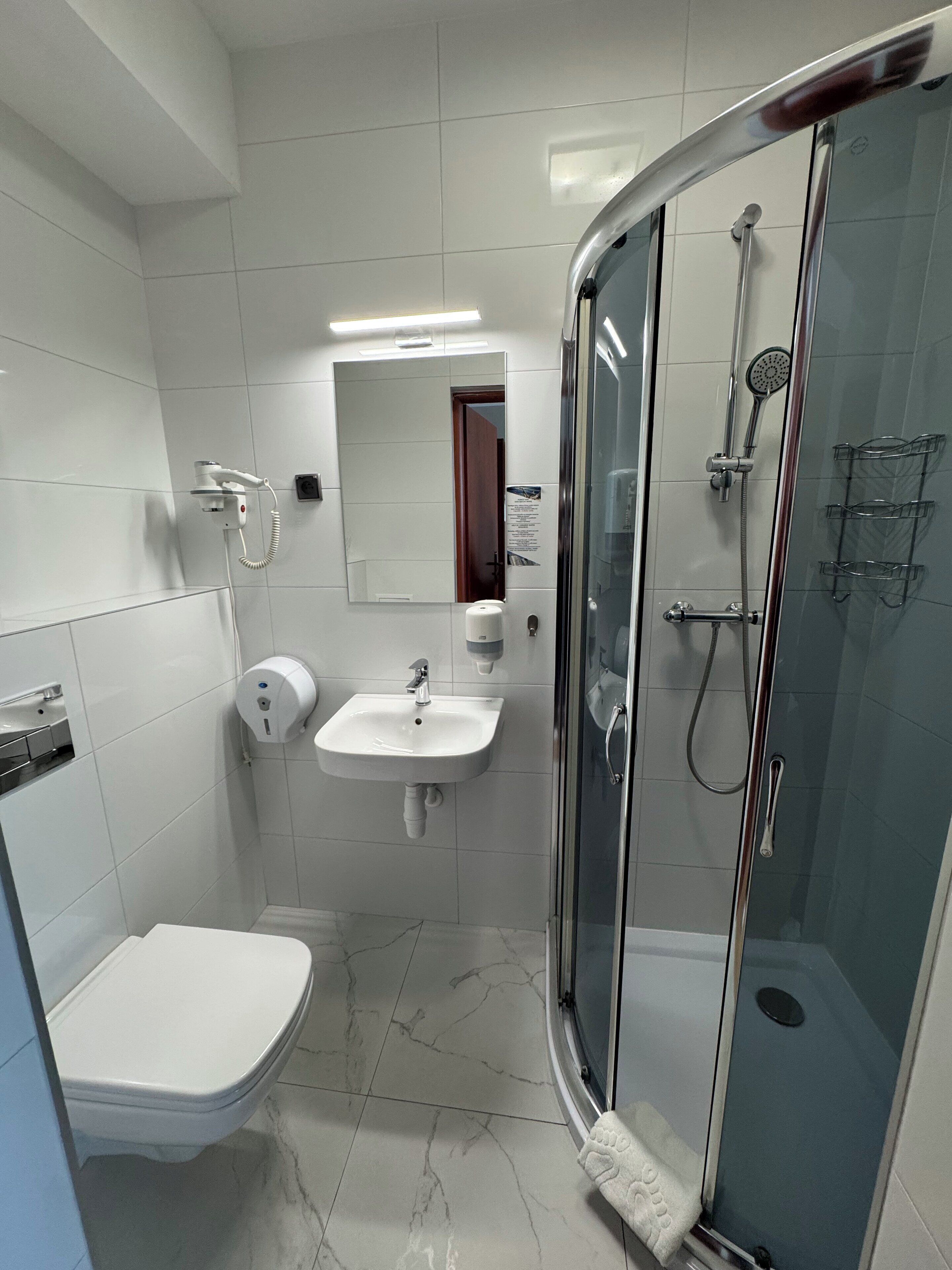 Un baño moderno con inodoro, lavamanos y ducha con mampara de vidrio.