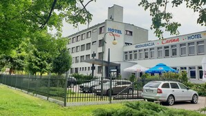 A hotel named "Carina" with a modern facade, a fenced parking area, and outdoor seating with umbrellas. - Hotel Carina (Tczew)