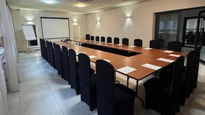 A conference room with a long table, black chairs, a whiteboard, and a projector screen. - Hotel Carina (Tczew)