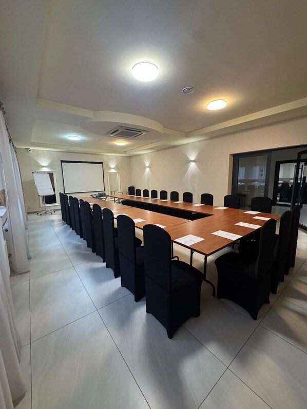 A conference room with a long table, black chairs, a whiteboard, and a projector screen.