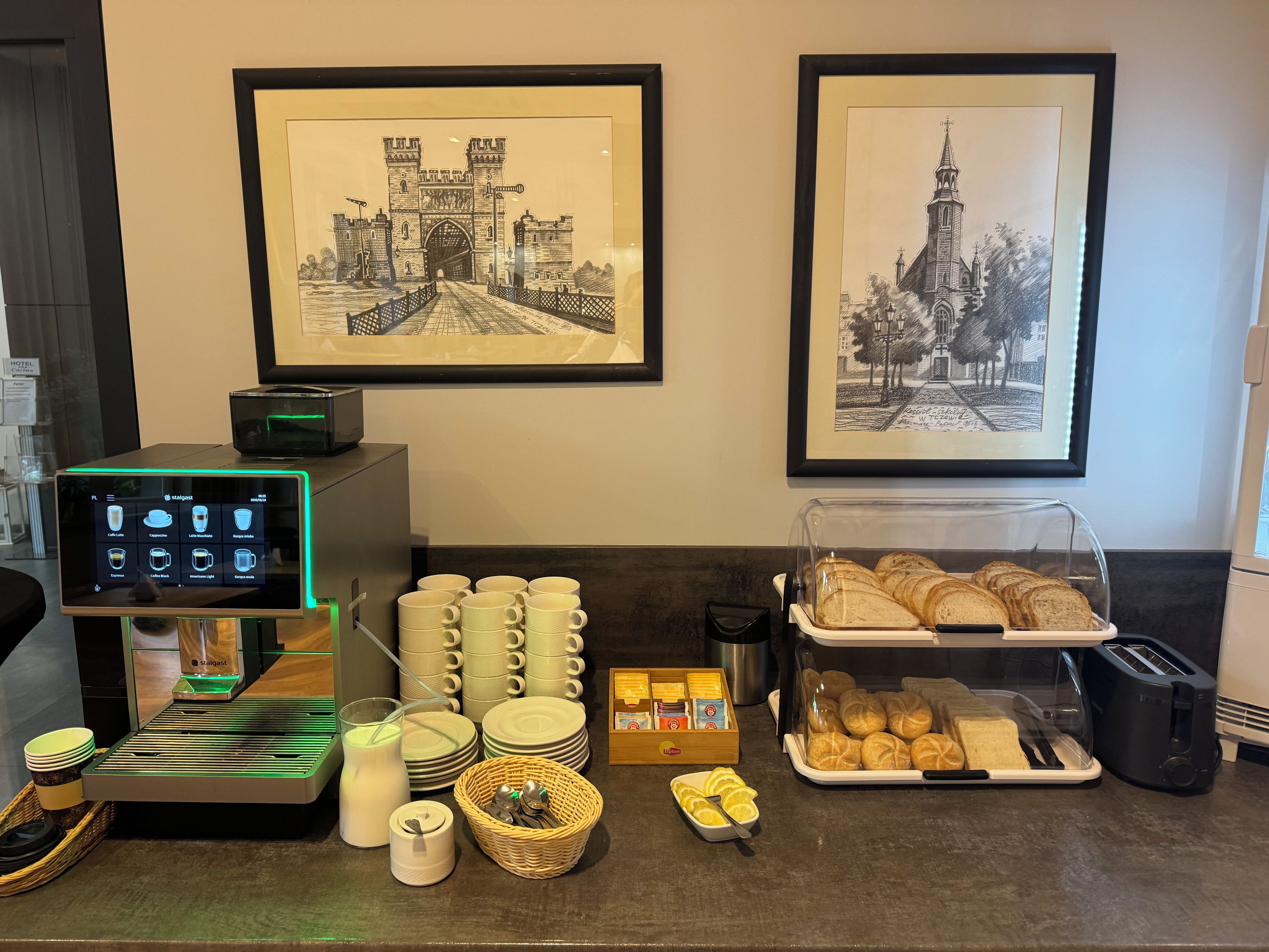 A breakfast buffet setup with a coffee machine, milk dispensers, and a bread display.
