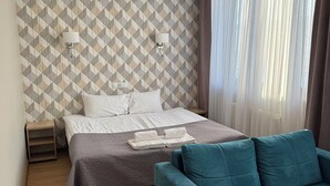 A hotel room with a bed, a nightstand, a teal sofa, and a patterned wall. - Hotel Carina (Tczew)