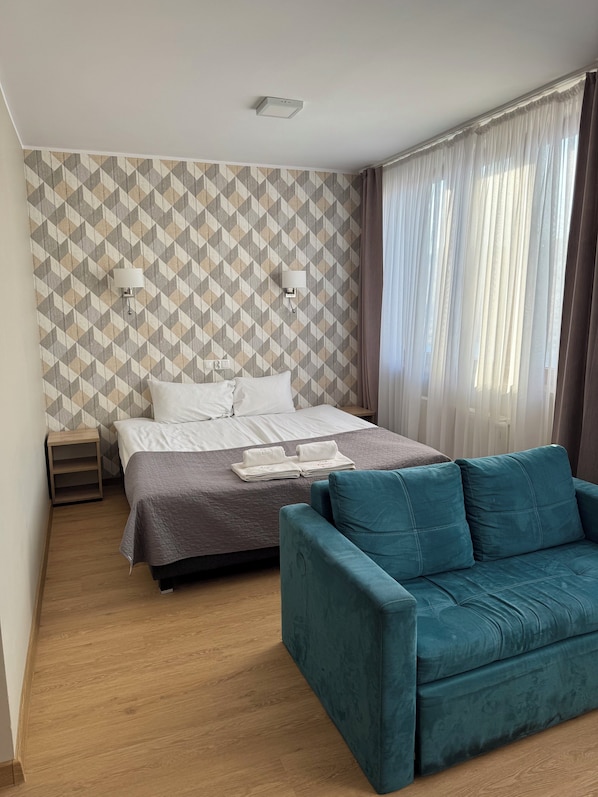 A hotel room with a bed, a nightstand, a teal sofa, and a patterned wall. - Hotel Carina (Tczew)