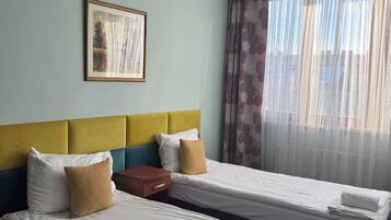 Een hotelkamer met twee bedden, een lijst met een foto aan de muur en dunne gordijnen voor het raam.