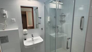 A modern bathroom with a glass-enclosed shower, a white sink, and a mirror above it.