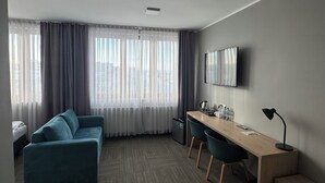 A modern hotel room with a sofa, a desk, and a TV. - Hotel Carina (Tczew)