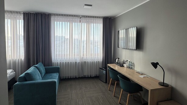 A modern hotel room with a sofa, a desk, and a TV. - Hotel Carina (Tczew)