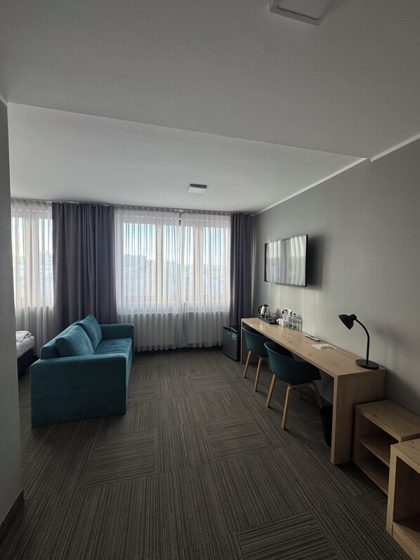 A modern hotel room with a sofa, a desk, and a TV. - Hotel Carina (Tczew)