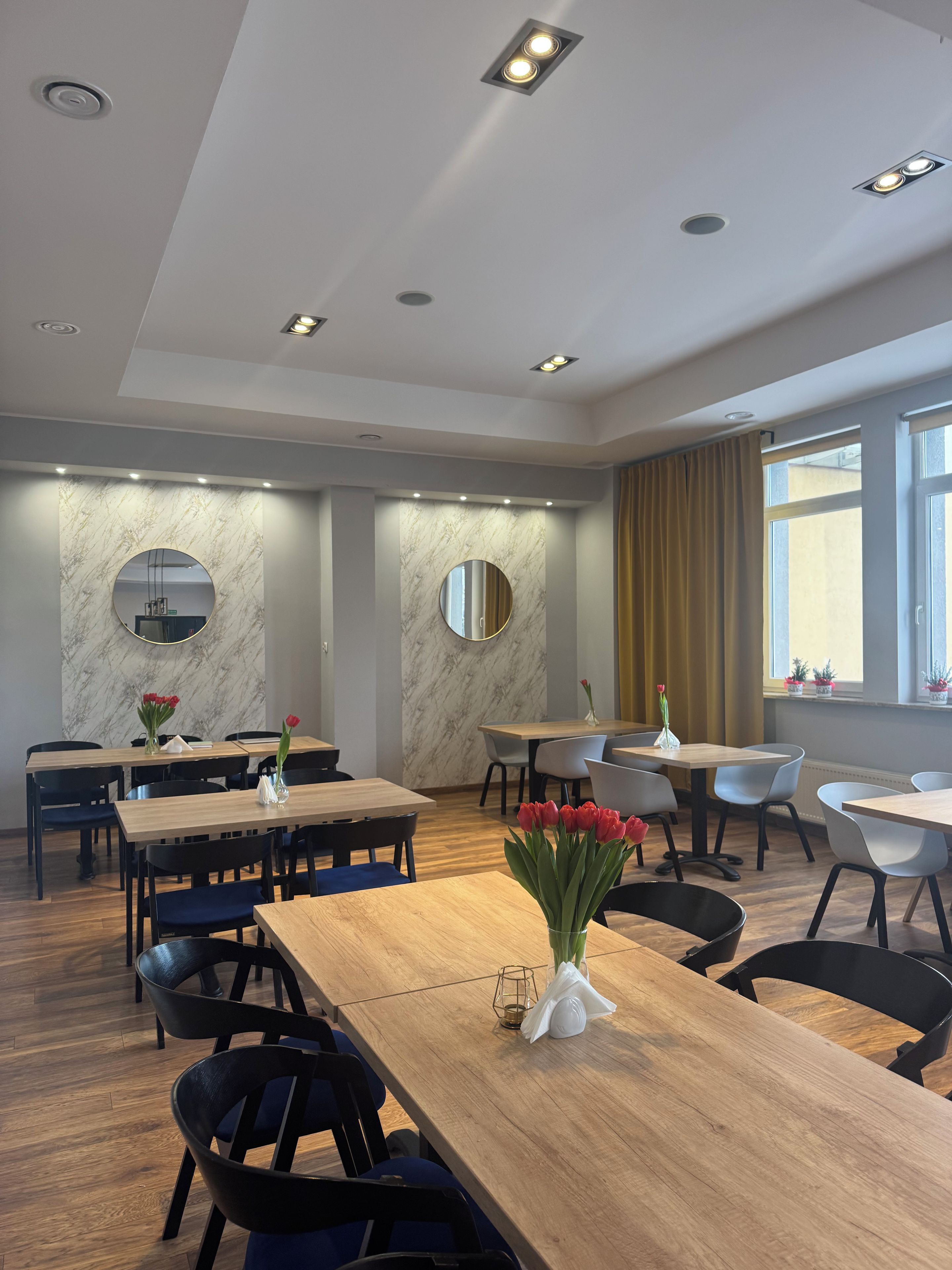 A modern dining area with round tables, chairs, and a vase of red flowers.