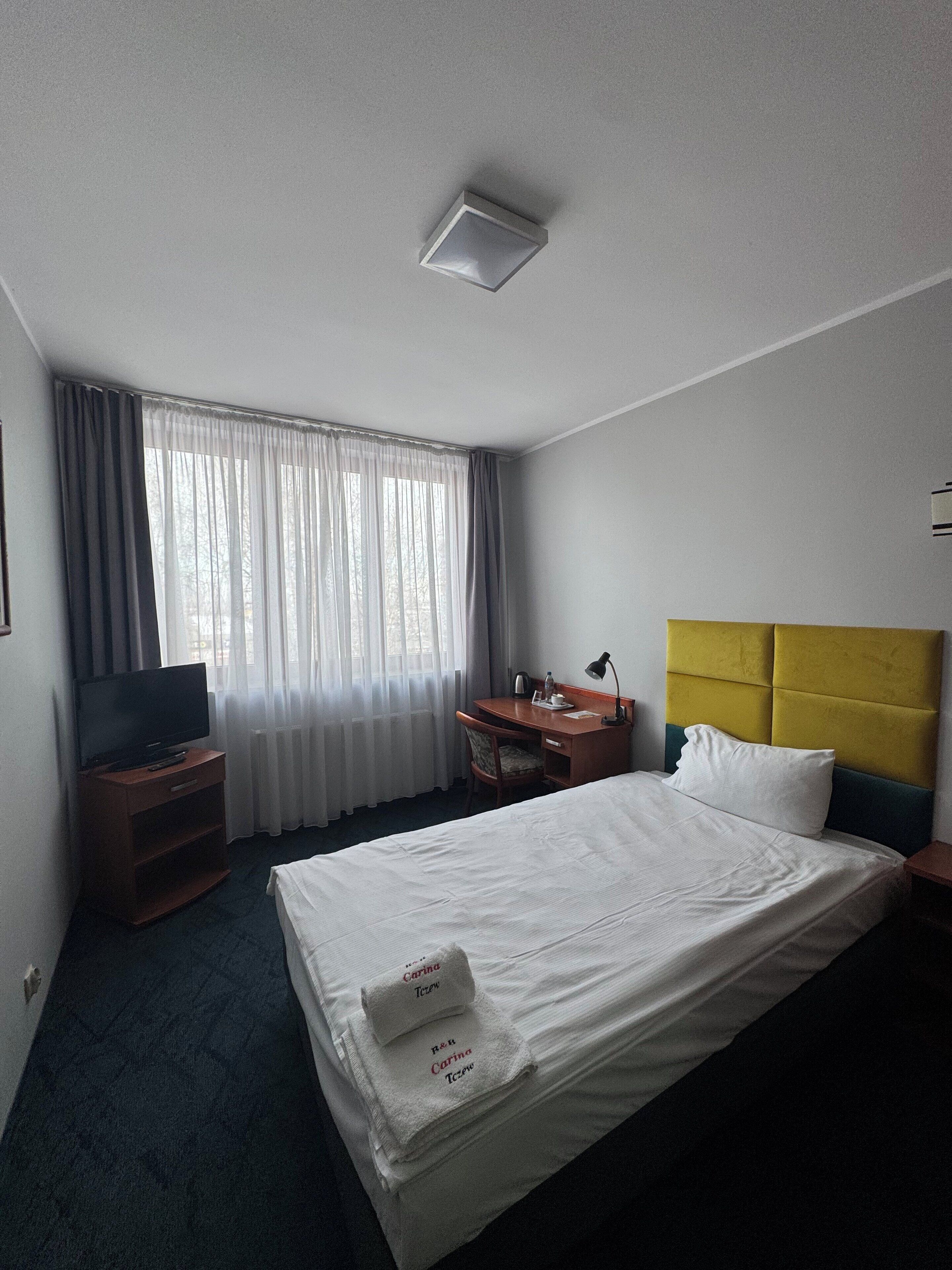 Ein Hotelzimmer mit Bett, Schreibtisch, Fernseher und einem Fenster mit Vorhängen.